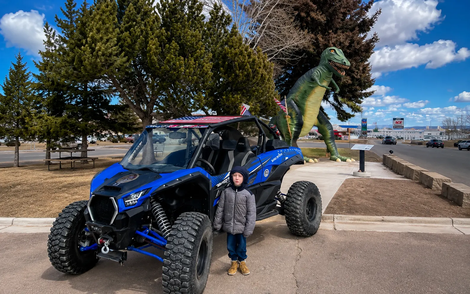 A child beside a Kawasaki KRX 1000 and the giant roadside dinosaur statue in downtown Vernal, Utah